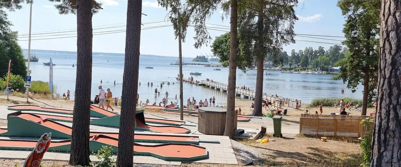 Minigolfbana vid Engesbergs camping. Många badar och solar vid vattnet, en brygga leder ut i sjön.