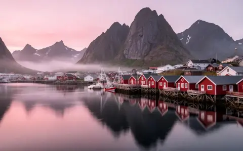 Röda fiskestugor vid vattnet i Lofoten, med berg och rosa himmel. En dröm om norrsken.