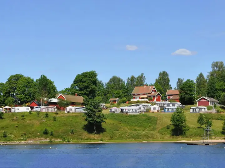 Gröna kullar med husbilar och röda stugor vid en sjö. En idyllisk plats för greans camping.