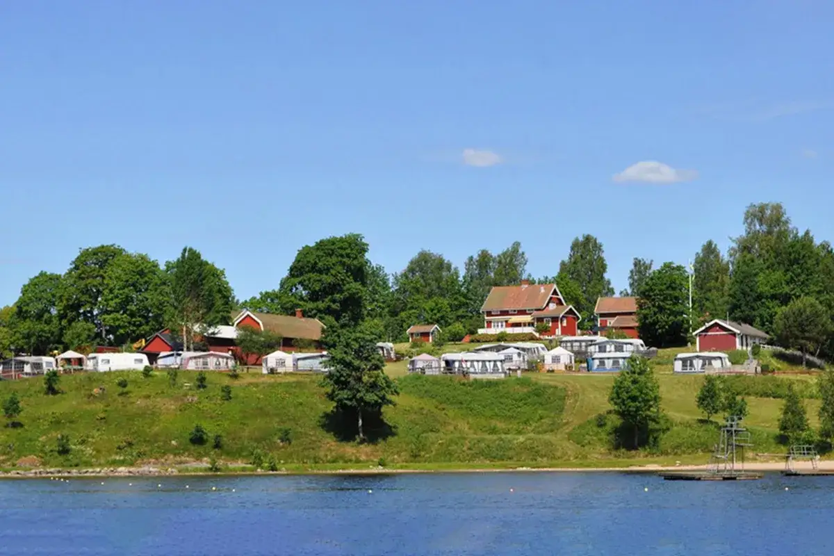 Gröna kullar med husvagnar och röda stugor vid en sjö, en idyllisk plats för greans camping.
