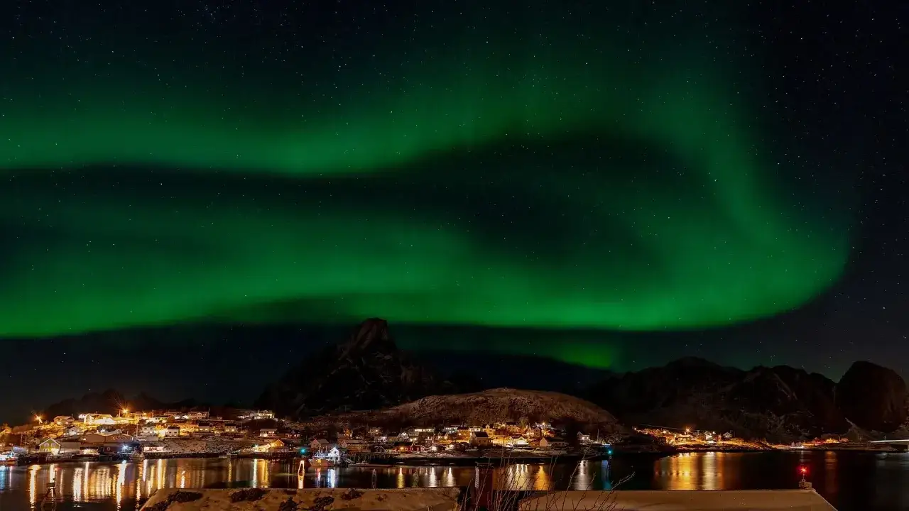 Magiskt norrsken &ouml;ver en by vid vattnet p&aring; Lofoten. En dr&ouml;m att se detta ljusspel.