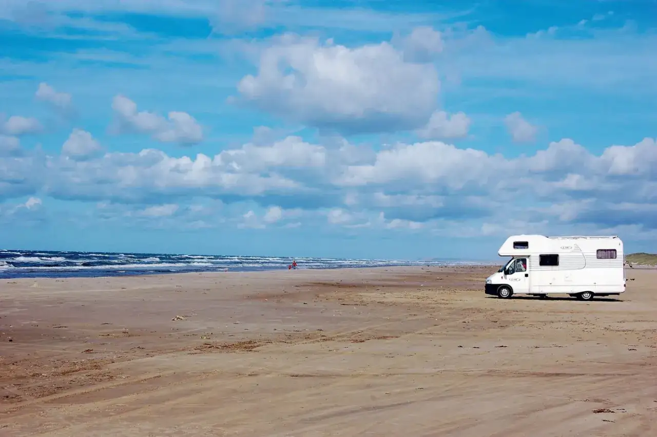 Husbil på en sandstrand vid havet. En person syns i fjärran. En perfekt plats att besöka Jylland på.