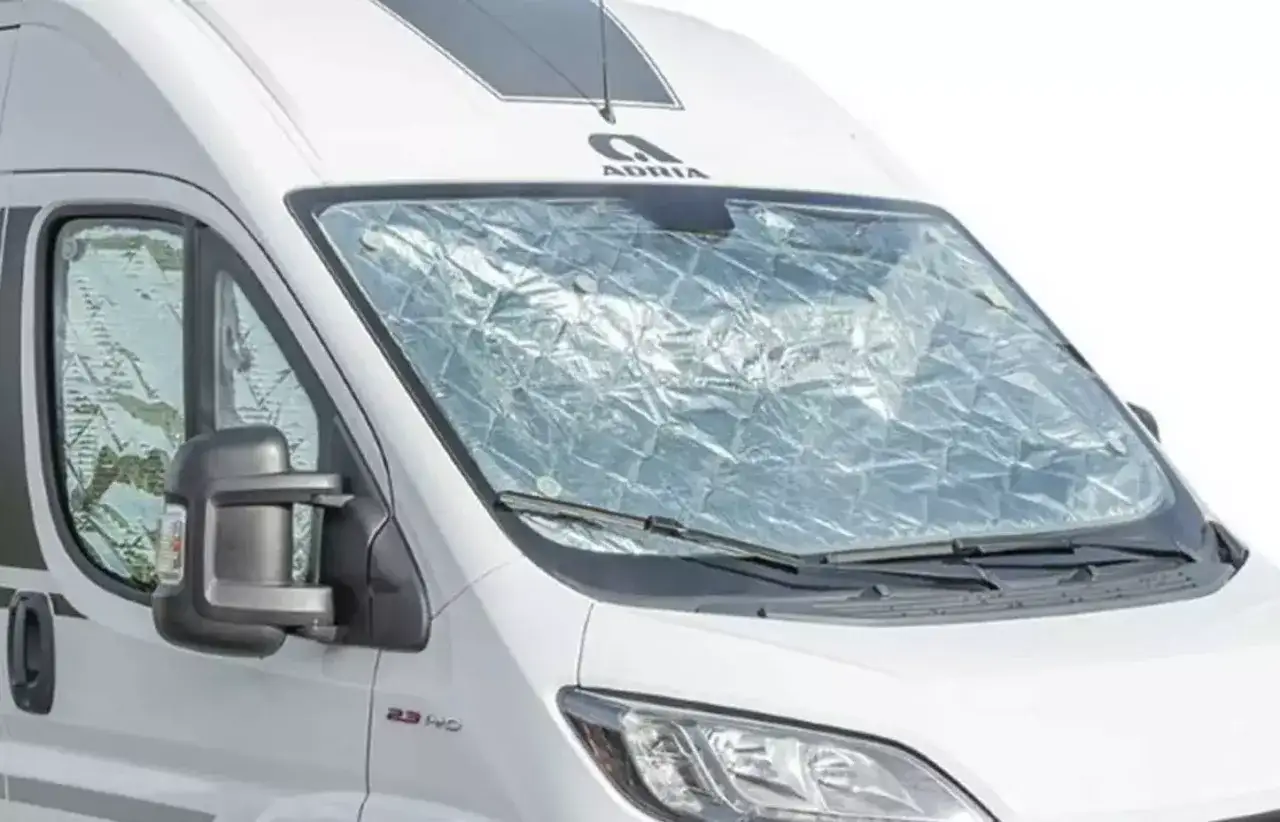 En vit husbil med en reflekterande vindrutetäckning, som en del av en truma frostvakt manual.