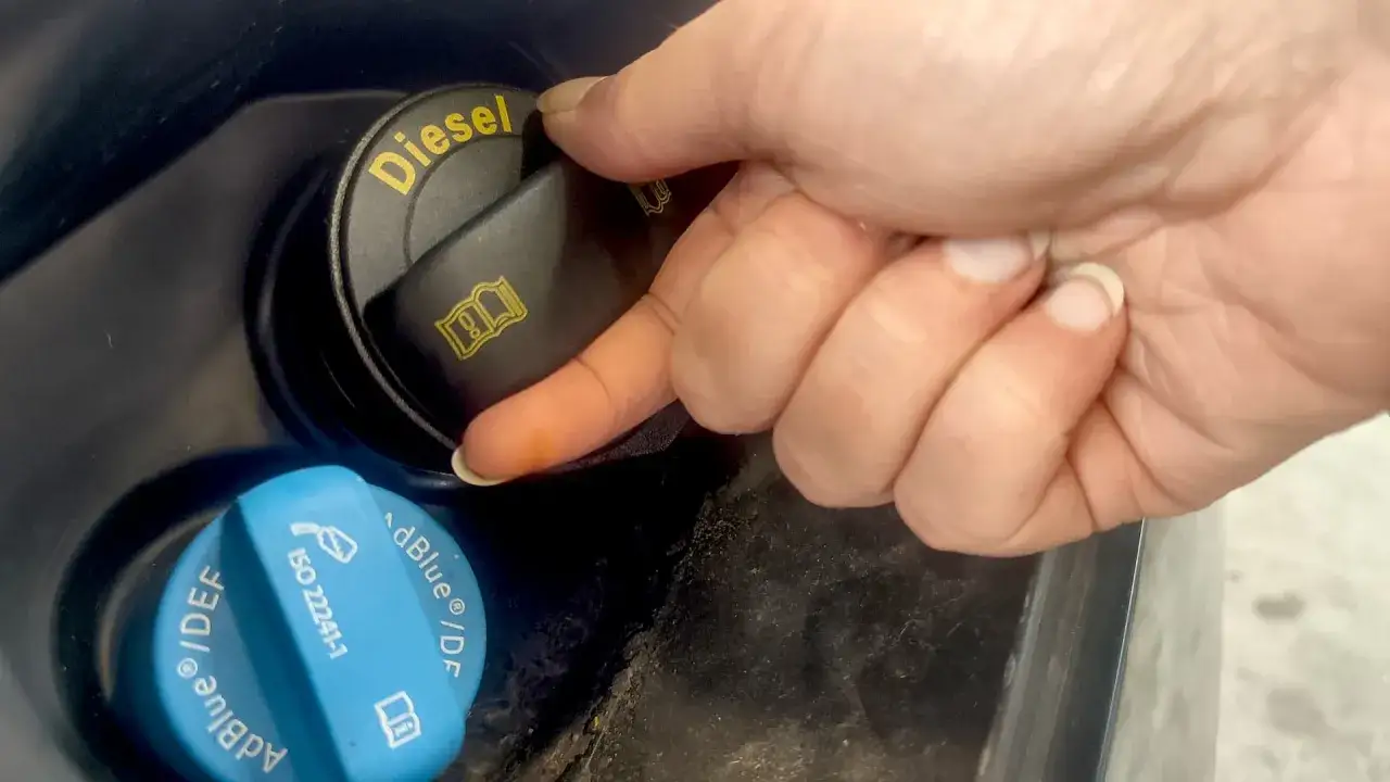 En hand skruvar p&aring; en svart dieselbeh&aring;llare. Bredvid finns en bl&aring; AdBlue-beh&aring;llare, viktig f&ouml;r att undvika problem med adblue fryspunkt.