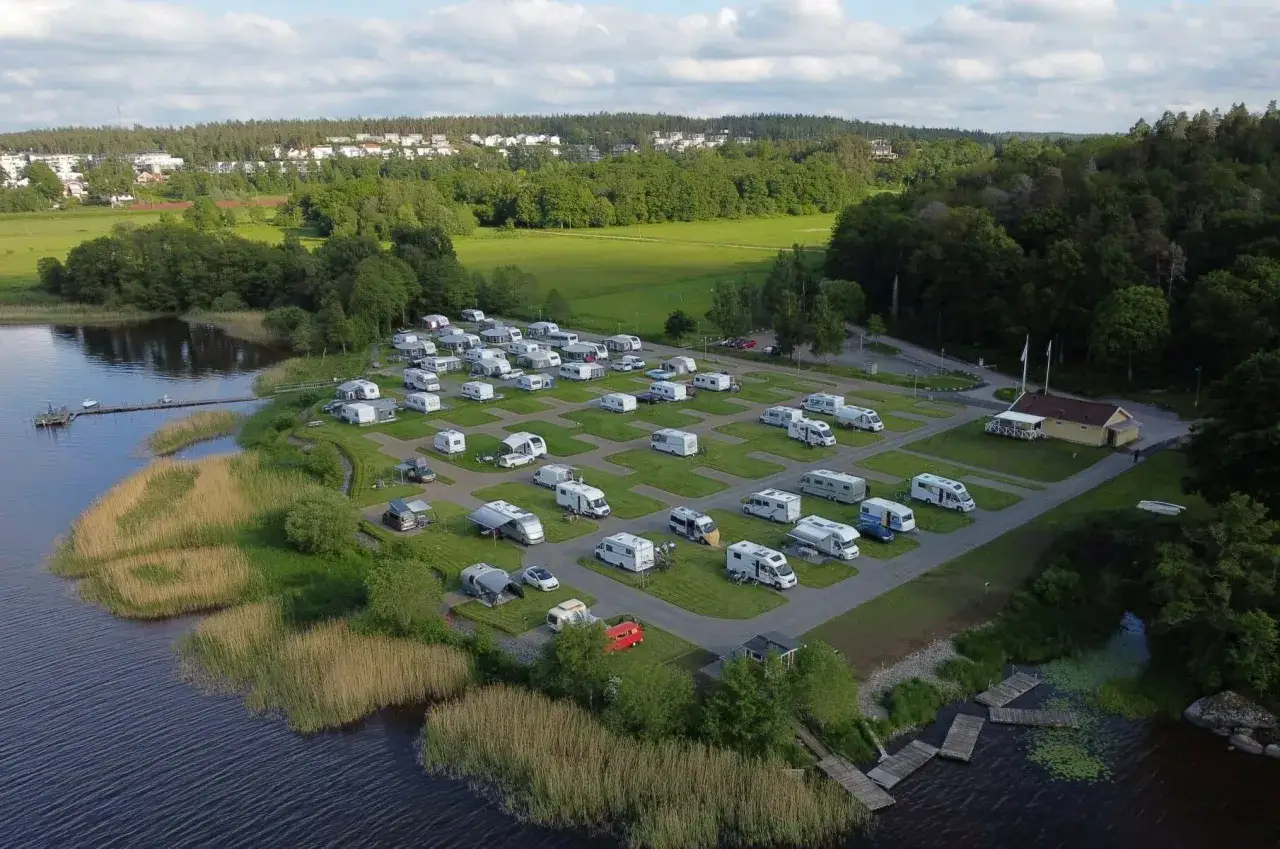 En campingplats vid en sj&ouml; n&auml;ra Alings&aring;s, med m&aring;nga husbilar och husvagnar uppst&auml;llda p&aring; gr&ouml;na platser.