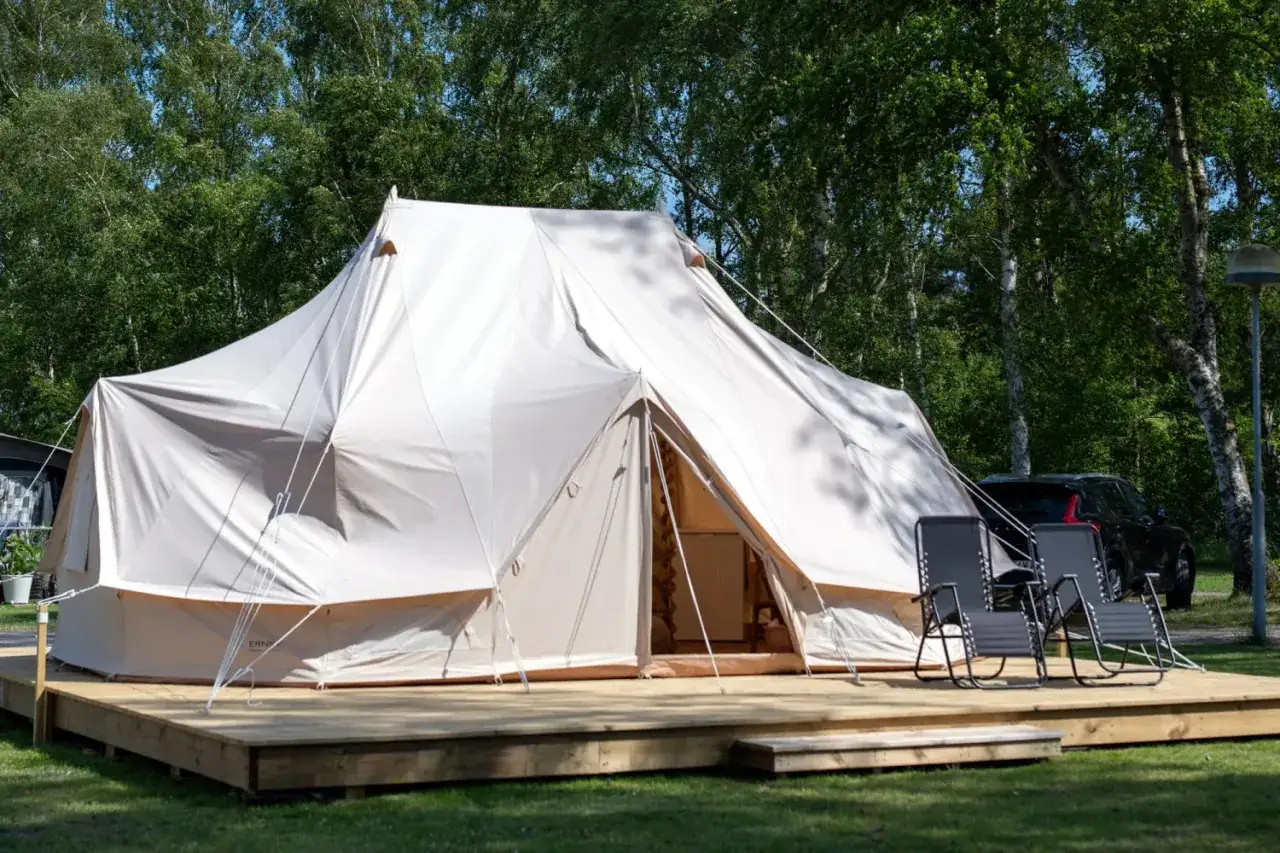 Stor glampingt&auml;lt p&aring; tr&auml;altan, redo f&ouml;r camping i Gnesta. Tv&aring; solstolar st&aring;r framf&ouml;r t&auml;ltet.