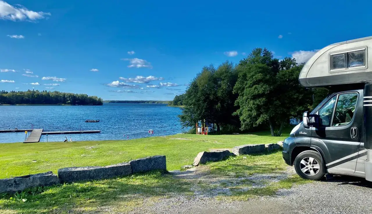 Husbil parkerad vid en sj&ouml; med brygga och gr&auml;smatta. En idyllisk plats f&ouml;r camping vid Alsterbro.