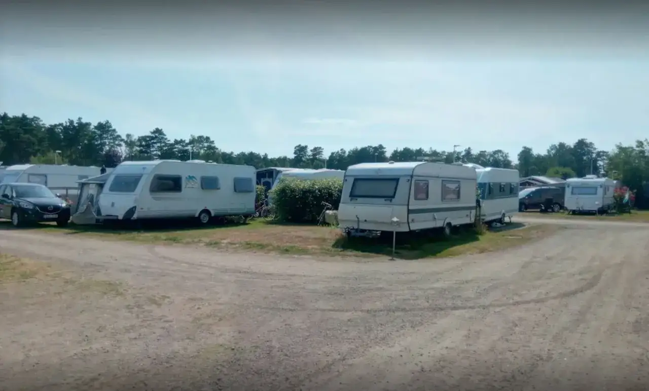 Ställplatser med husvagnar och bilar på Olles camping. Träd och blå himmel i bakgrunden.