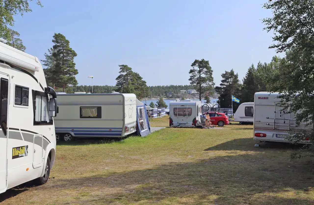 Solig dag på camping norrlandskusten med husbilar och husvagnar uppställda vid vattnet.