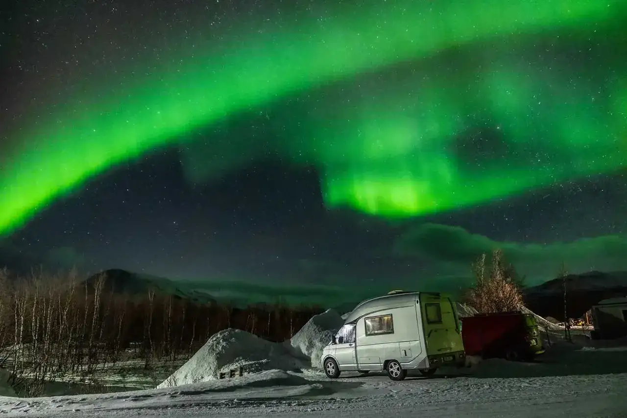 Grön norrsken dansar över en snöig finsk natt. En husbil står parkerad, redo för äventyr under stjärnorna.