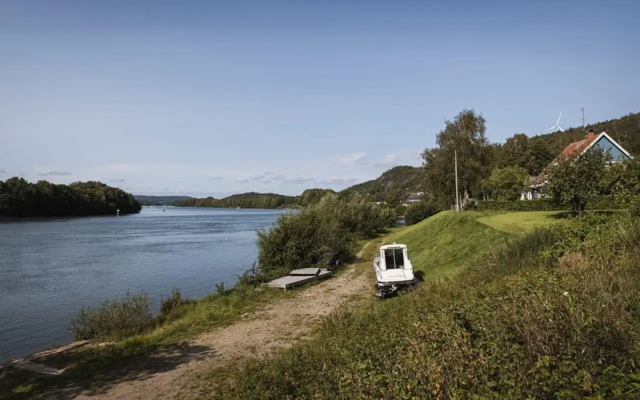 En vacker dag vid vattnet nära camping Lilla Edet. En vit båt står parkerad vid en grusväg, redo för äventyr på sjön.