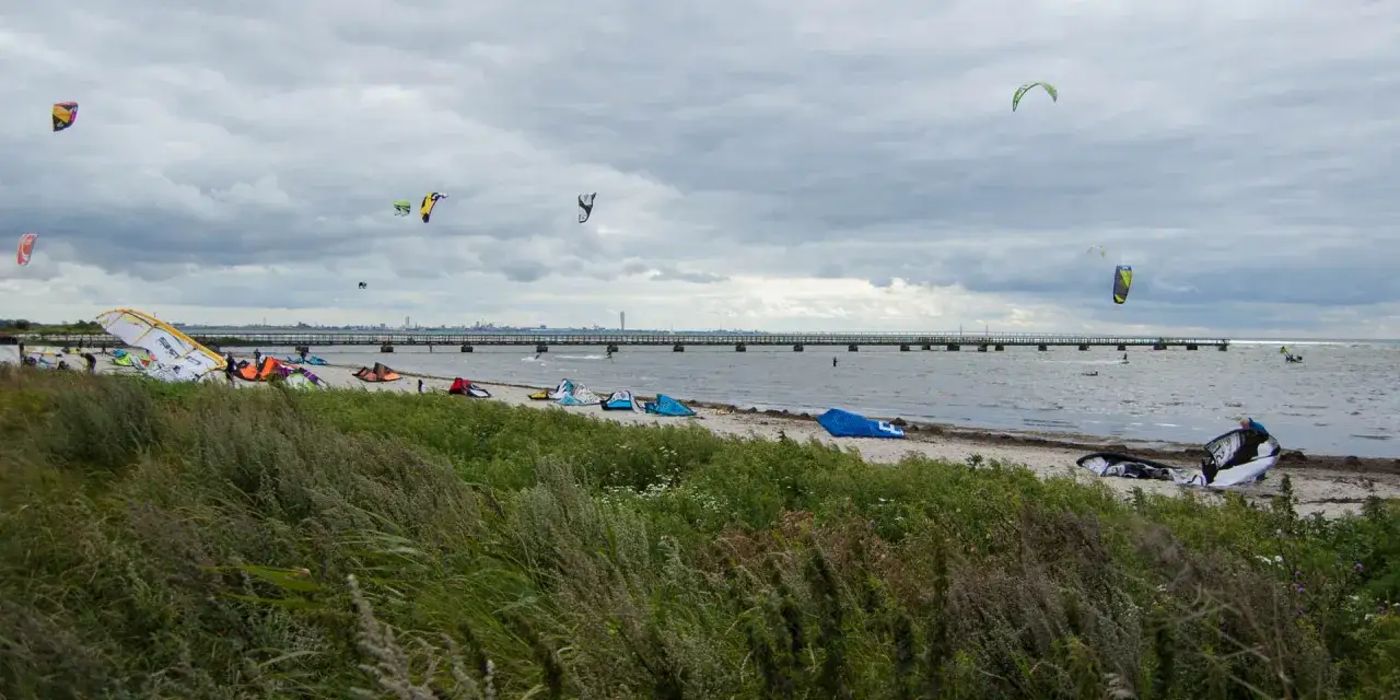Kitesurfare f&ouml;rbereder sig vid Habo Ljung Camping. M&aring;nga drakar och utrustning ligger p&aring; stranden, n&aring;gra flyger i luften.