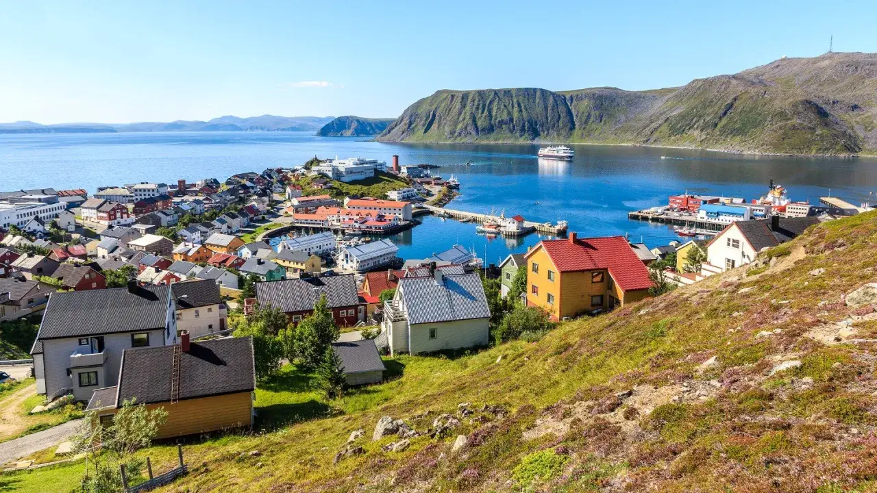 Färgglada hus i en kuststad vid en fjord, med ett stort fartyg i bakgrunden. Detta är Norges nordligaste stad, Honningsvåg.