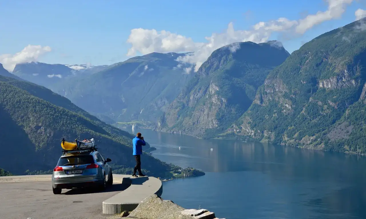 En man fotograferar en fjord under sin semester i Norge. Bilen p&aring; taket har kajaker redo f&ouml;r &auml;ventyr.