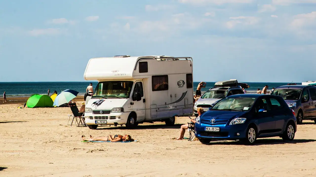 Solig stranddag på Jylland med husbil, bilar, tält och solbadare.